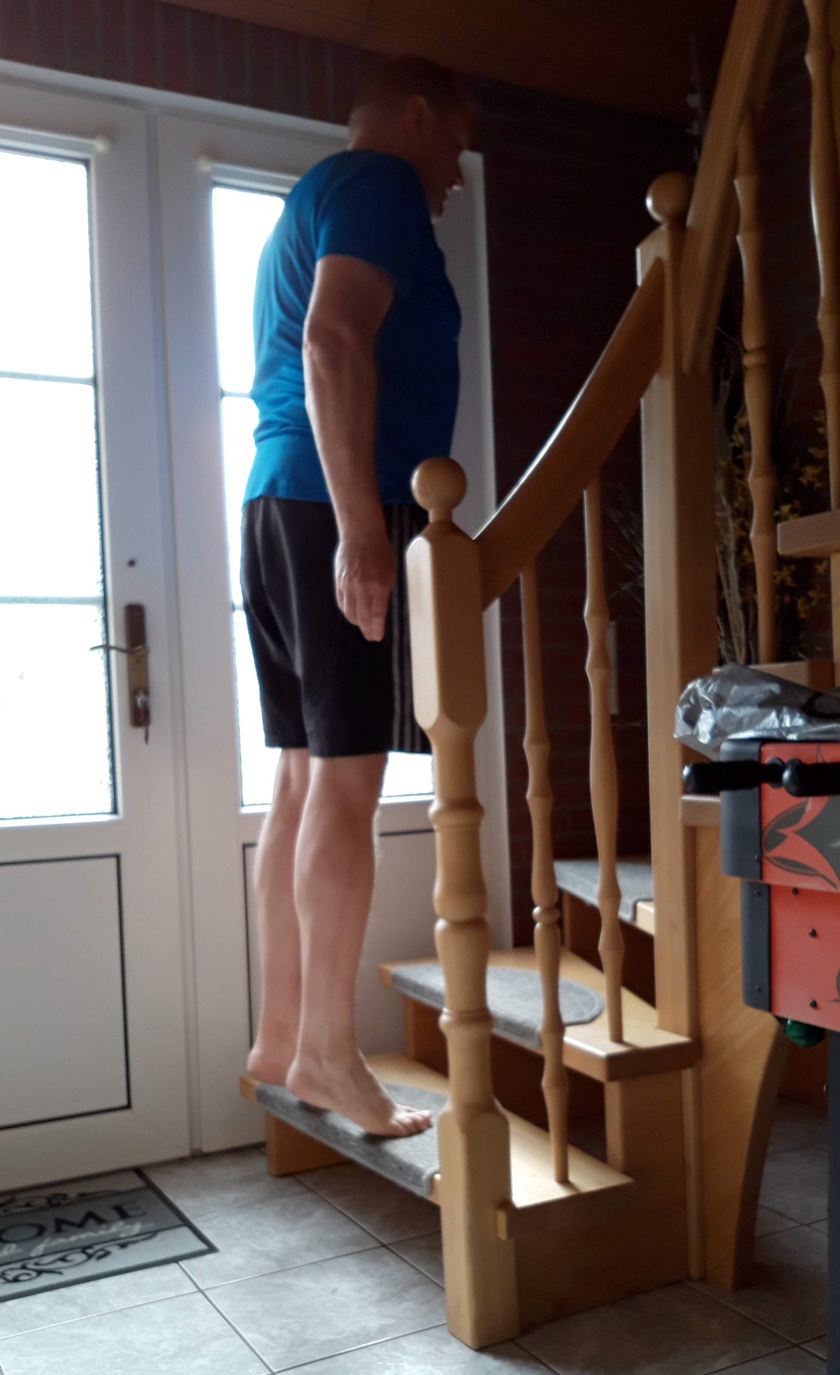 Mann in sportlichem Dress führt auf einer normalen Treppe das Wadenheben durch. 